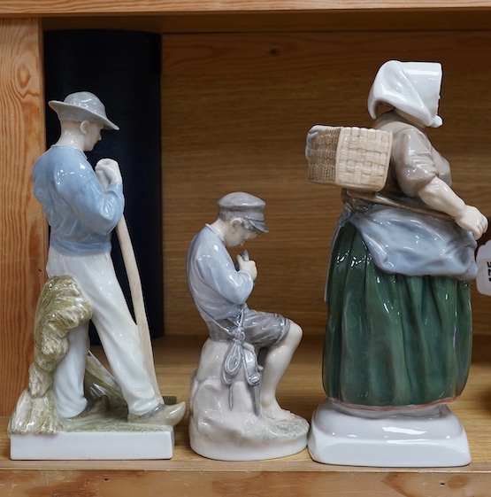 Two Royal Copenhagen figures of a farmer holding a scythe, model number 685, a boy whittling a stick, model 905, together with a Bing and Grondahl figure of a woman, model number 1702, tallest 28cm (3). Condition - good